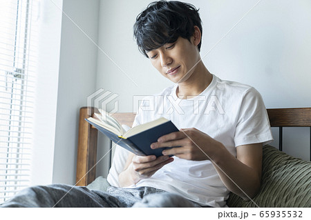 ベッド に座って本を読む若い男性の写真素材