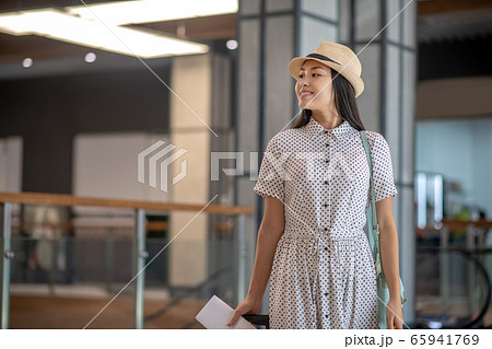 Brunette female in straw hat standing with tickets and suitcase, smiling Brunette female in straw hat standing with tickets and suitcase, smiling 65941769