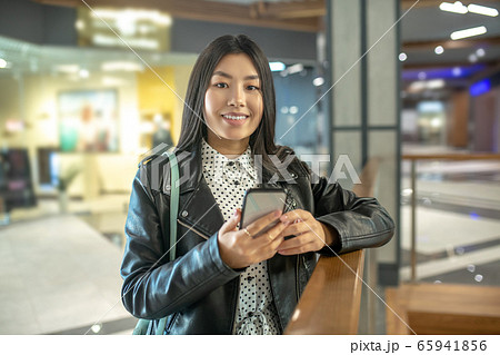 Young brunette female leaning on stair rails, holding her smartphone, smiling 65941856
