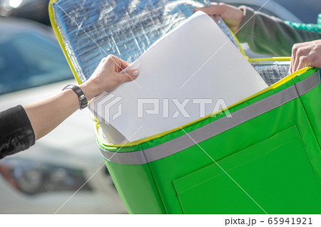 Close-up of male courier hands holding cooler bag and female hands taking the paper bag Close-up of male courier hands holding cooler bag and female hands taking the paper bag 65941921