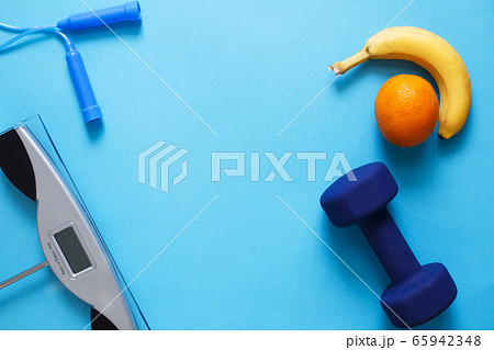 Flat lay composition with weigh scales, skipping rope and dumbbells isolated on a blue background. Healthy active lifestyle Flat lay composition with weigh scales, skipping rope and dumbbells isolated on a blue background. Healthy active lifestyle 65942348