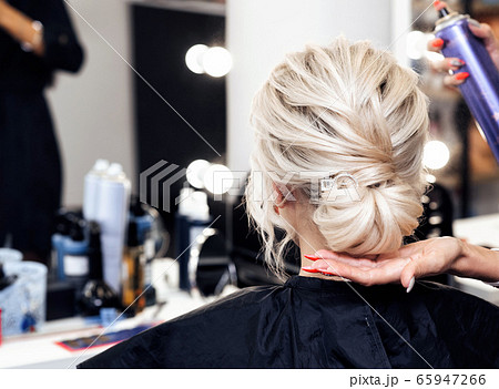 hairdresser makes his own hands hairstyle a bun on the head of a blonde girl 65947266