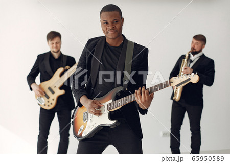 Black man in black suit standing with a guitar 65950589