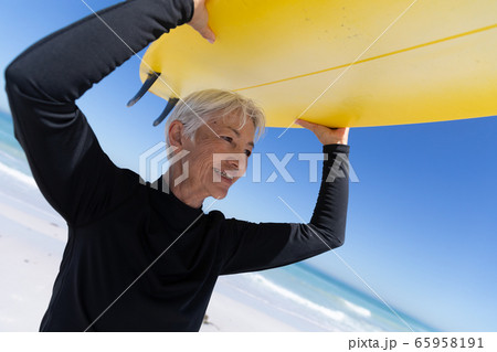 Senior Caucasian woman holding a surfboard at the beach. 65958191