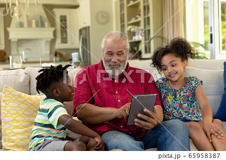 Senior mixed race man sitting on the couch with his young grandson and granddaughter 65958387