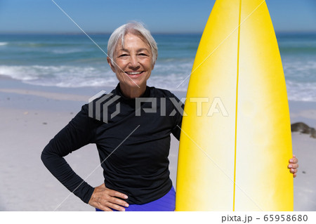 Senior Caucasian woman holding a surfboard at the beach. Senior Caucasian woman holding a surfboard at the beach. 65958680