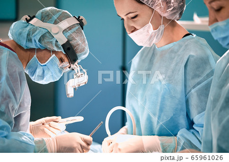Modern surgery in a technologically advanced hospital. Bright room of intensive care. Doctors and assistants working in the operating room save lives. Modern surgery in a technologically advanced hospital. Bright room of intensive care. Doctors and assistants working in the operating room save lives. 65961026