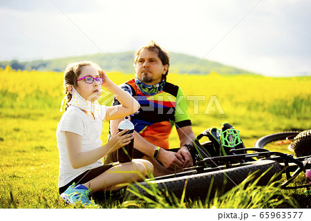 Sport and quarantine. 9 years girl ciclist with father having rest breathing without masks admist the fields in the sunny day 65963577