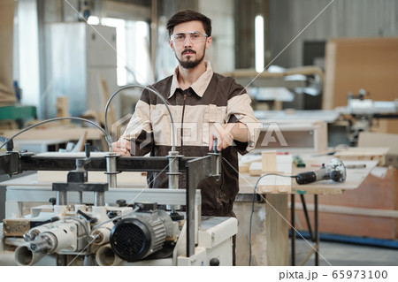 Young serious worker of factory standing by workbench during processing work 65973100