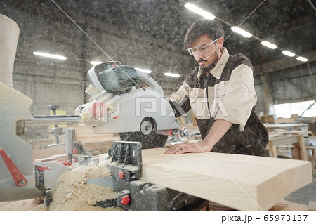 Young worker of furniture production factory using electric saw at work 65973137