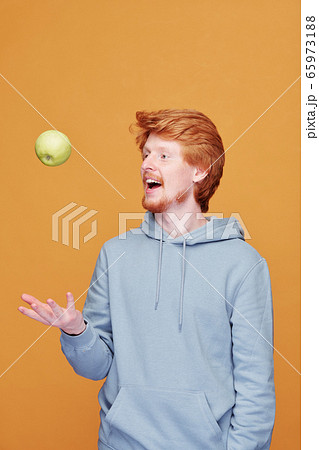 Happy young casual man throwing green apple in front of himself while having fun 65973188