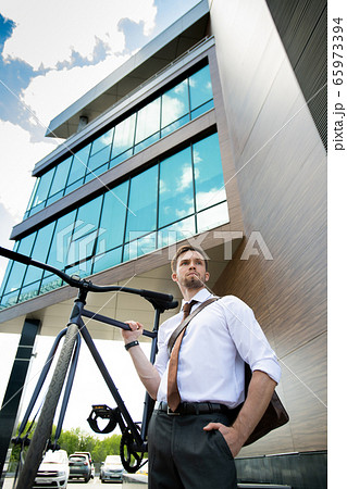 Young handsome businessman holding bicycle while standing in urban environment Young handsome businessman holding bicycle while standing in urban environment 65973394