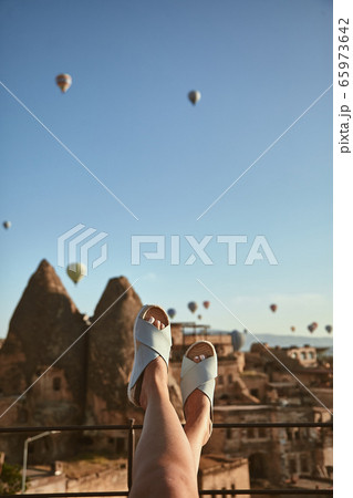 Find your escape. Close up of feet of woman sitting on one of the top roofs, enjoying the spectacular view of flying balloons in Cappadocia, Turkey Find your escape. Close up of feet of woman sitting on one of the top roofs, enjoying the spectacular view of flying balloons in Cappadocia, Turkey 65973642