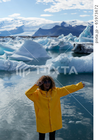 Enjoying Icelandic nature. Excited female tourist in yellow jacket visiting Jokulsarlon glacier lagoon in Iceland. She is looking at camera and smiling Enjoying Icelandic nature. Excited female tourist in yellow jacket visiting Jokulsarlon glacier lagoon in Iceland. She is looking at camera and smiling 65973672