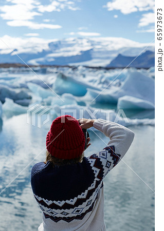 Exploring beautiful Icelandic nature. Young girl, female tourist or photographer taking a photo of floating ice in Jokulsarlon glacier lagoon in Iceland Exploring beautiful Icelandic nature. Young girl, female tourist or photographer taking a photo of floating ice in Jokulsarlon glacier lagoon in Iceland 65973673