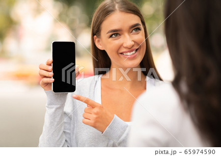 Girl Showing Phone Empty Screen To Friend Walking In Park 65974590