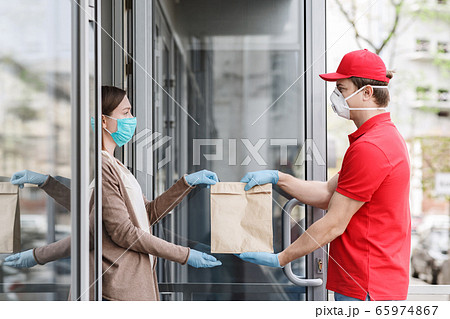 Courier in medical mask and gloves transfers package to customer at home. Courier in medical mask and gloves transfers package to customer at home. 65974867