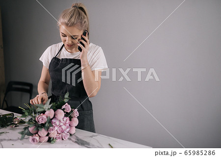 Young business woman florist wearing apron talking on mobile phone with client 65985286