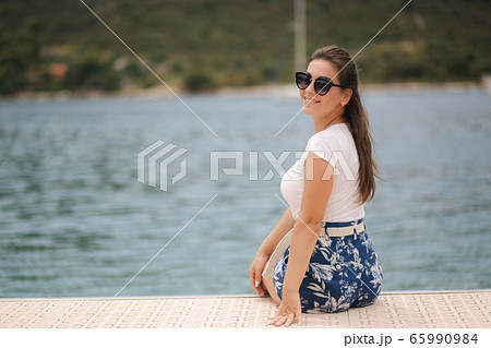 Back view of young woman woman sits alone on the pier by the sea. Happy woman 65990984
