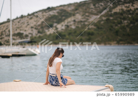 Back view of young woman woman sits alone on the pier by the sea. Happy woman 65990989