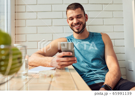 Cheerful young man using mobile phone at home 65991139