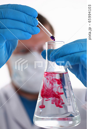 A male chemist holds test tube of glass in his hand overflows a liquid 65994103