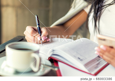 Young woman right hand writing plans on small diary in cafe close up Young woman right hand writing plans on small diary in cafe close up 66003386