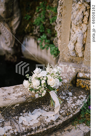 White bride bouquet with silk ribbons on an old fountain. White bride bouquet with silk ribbons on an old fountain. 66008162