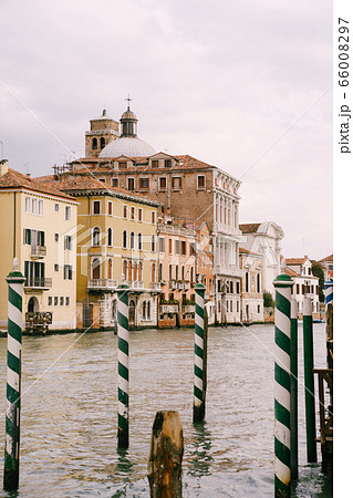 View of the buildings on the Grand Canal, Venice, Italy, through green striped poles - a pier for gondolas and boats. 66008297