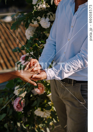 Interracial wedding couple - African-American bride and Caucasian groom. Groom puts a ring on brides finger. Destination fine-art wedding in Florence, Italy. Wedding ceremony on the roof Interracial wedding couple - African-American bride and Caucasian groom. Groom puts a ring on brides finger. Destination fine-art wedding in Florence, Italy. Wedding ceremony on the roof 66008575