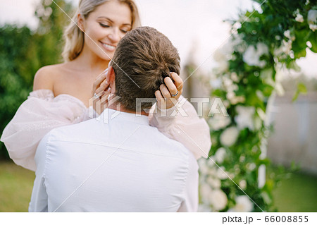 Wedding at an old winery villa in Tuscany, Italy. The groom holds the bride in his arms. Round wedding arch decorated with white flowers and greenery in front of an ancient Italian architecture. 66008855