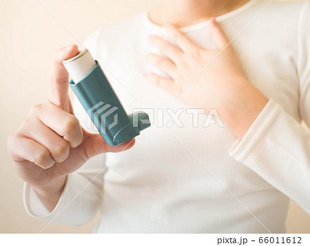 Young female in white t-shirt using blue asthma inhaler for relief asthma attack. Pharmaceutical products is used to prevent and treat wheezing and shortness of breath caused asthma or COPD. Close up. Young female in white t-shirt using blue asthma inhaler for relief asthma attack. Pharmaceutical products is used to prevent and treat wheezing and shortness of breath caused asthma or COPD. Close up. 66011612