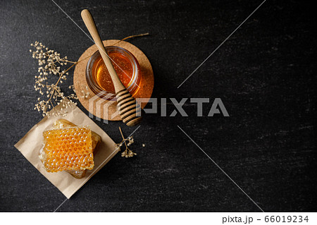 Honey bee and Honeycomb with honey dipper and dry flower on black background, bee products by organic natural ingredients concept Honey bee and Honeycomb with honey dipper and dry flower on black background, bee products by organic natural ingredients concept 66019234