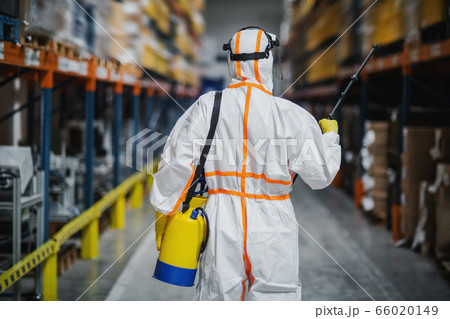 Rear view of man worker with protective suit disinfecting industrial factory with spray gun. 66020149
