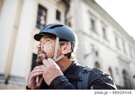 Delivery man courier fastening bicycle helmet in town. Delivery man courier fastening bicycle helmet in town. 66020416