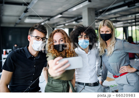 Young people with face masks back at work in office after lockdown, taking selfie. 66020983