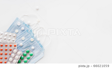 Top view on pack of blue protective medical masks and different scattering pills. Coronavirus COVID-19 concept on  white background with copy space. 66021059