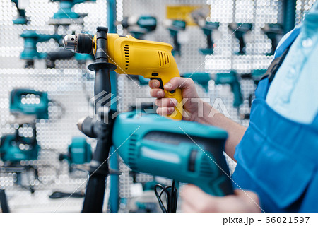 Worker holds two electric drills in tool store Worker holds two electric drills in tool store 66021597