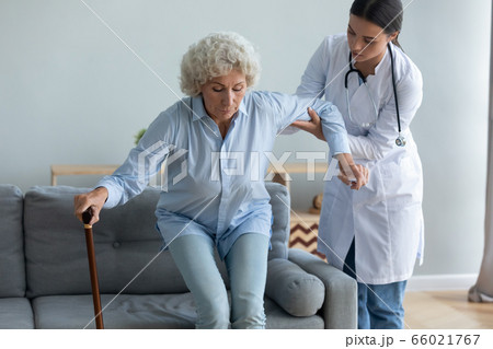 Caring nurse helping to elderly woman get off the couch 66021767