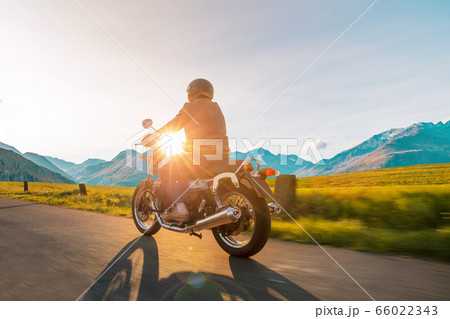 Motorcycle driver riding in Alpine highway, 66022343