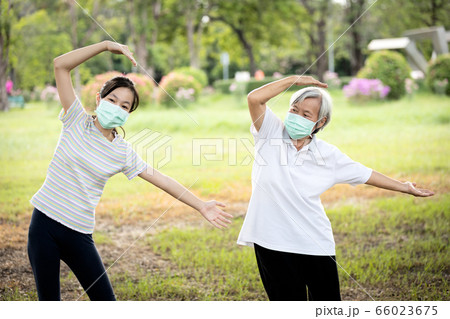 Happy child girl is doing exercise activity for the old elderly,healthy senior woman workout and wear face mask outside home after Coronavirus quarantine or Covid-19 lockdown,work out for health care 66023675