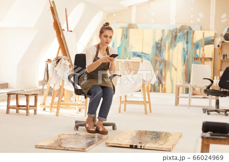 Female Artist Taking Photos of Paintings in Studio 66024969