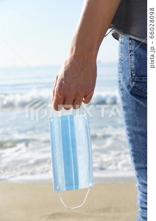 man with a surgical mask in his hand on the beach 66028098