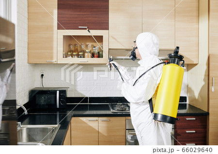 Worker in hazmat suit applying spray on surfaces 66029640