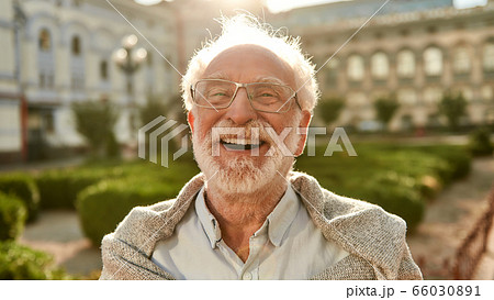 Don't stop laughing! Portrait of happy and handsome senior man in glasses looking at camera and smiling while standing outdoors on a sunny day 66030891