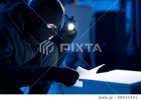 Masked intruder holding and reading confidential documents 66035441