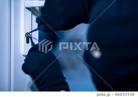 Robber in black mask cracking door with metal picklock 66035530