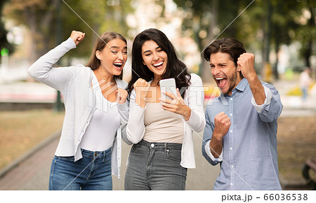 Three Joyful Friends With Cellphone Shaking Fists Celebrating Victory Outdoor Three Joyful Friends With Cellphone Shaking Fists Celebrating Victory Outdoor 66036538