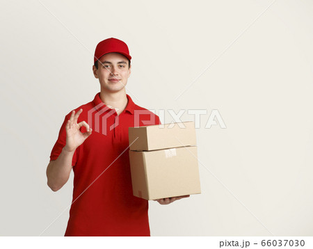 Friendly courier holds cardboard boxes and shows ok gesture 66037030