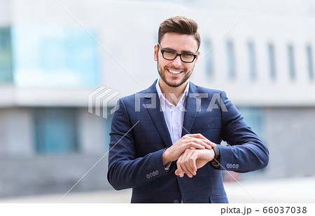 Smiling young CEO checking time on his wristwatch at city center, copy space Smiling young CEO checking time on his wristwatch at city center, copy space 66037038